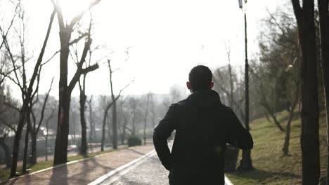 backside footage of male figure running in park. slow motion.