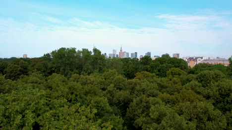 descending drone shot showing skyline of warsaw city and dense green forest in foreground - capital of poland during sunny day