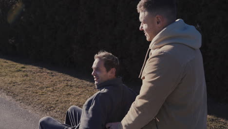 young man walking while pushing his disabled friend in wheelchair and talking together