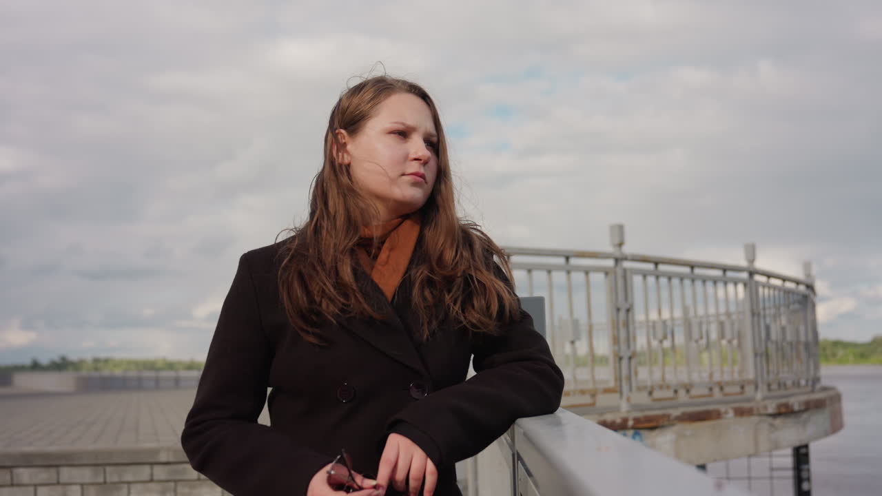 Female adult suddenly turns to camera and bursts out laugh while standing on bridge under hazy sky, wind moving hair softly, mood shifting from calm reflection to genuine joy and spontaneous emotion