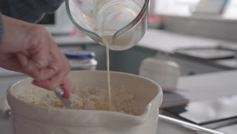 una dama haciendo masa en la cocina, vierte leche en la mezcla en un tazón de cerámica mientras revuelve