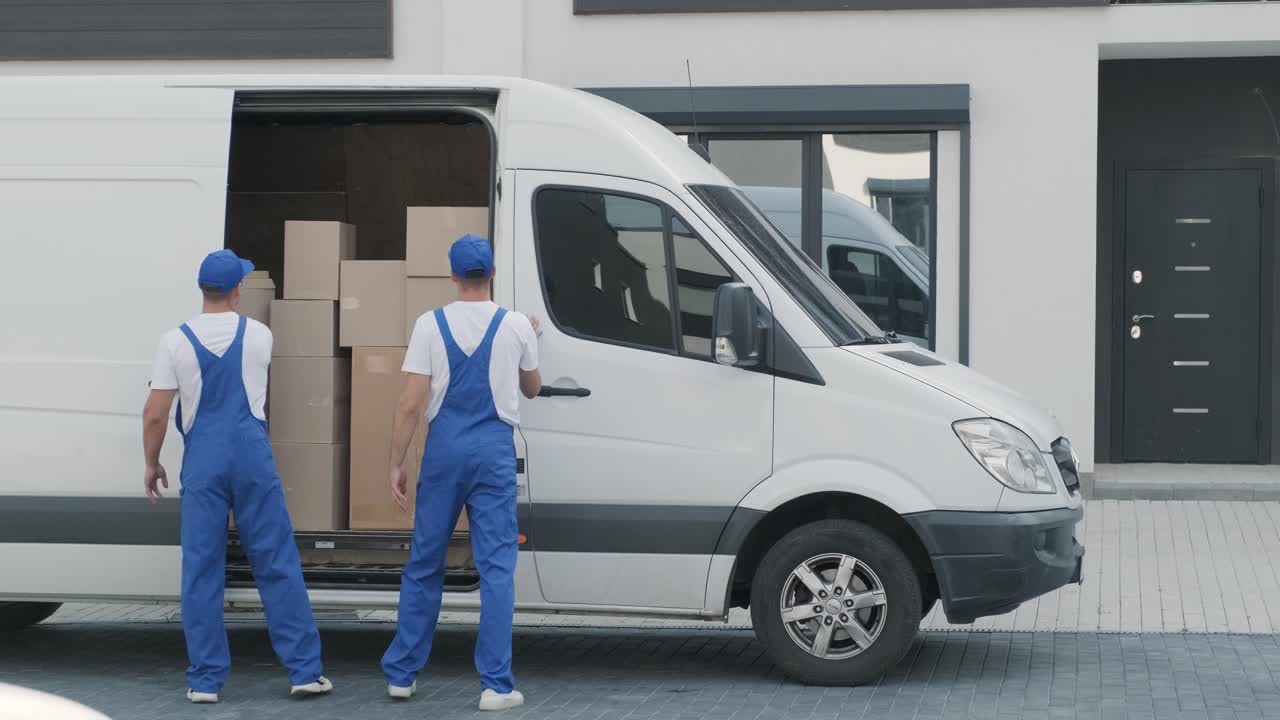 dos jóvenes trabajadores de una empresa de mudanzas descargan cajas del minibús en la casa del cliente