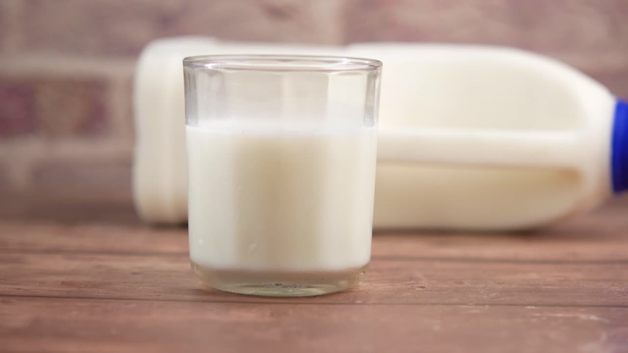 un vaso de leche junto a una jarra de un galón