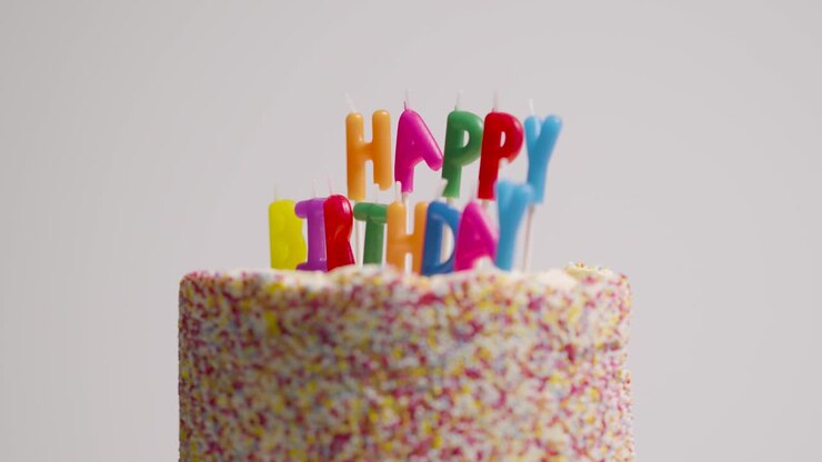 Studio Shot Of Revolving Birthday Cake Covered With Decorations And Candles Spelling Out Happy Birthday