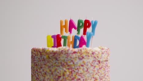 studio shot of revolving birthday cake covered with decorations and candles spelling out happy birthday