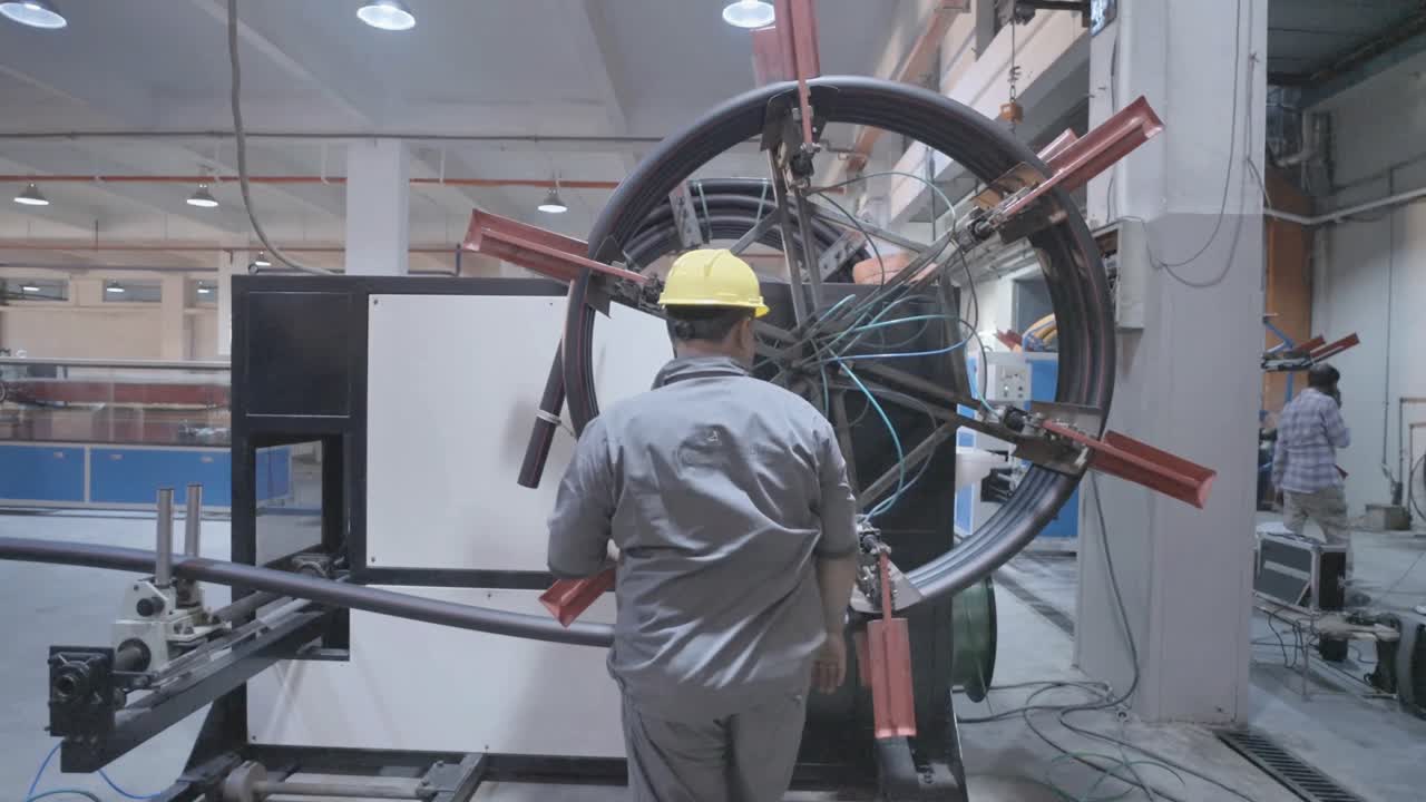 Back view of a worker rotating machine wheel to be used in PVC Pipe Making Factory in Karachi, Pakistan.