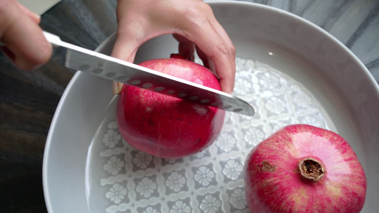 Kniv, der skærer igennem et granatæble, som ligger på en hvid tallerken på et bord. Med sunde antioxidanter og hjertebeskyttende egenskaber.