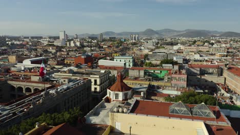 Toma-Aérea-De-La-Ciudad-De-México,-Pedestal-Abajo-Con-Bandera-Mexicana-Ondeando-En-El-Viento