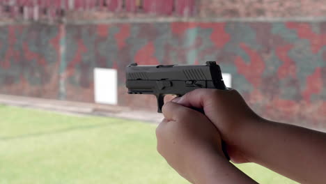 slow motion scenes of the gun firing at a shooting range on the man hand withhold the gun tight and pull the trigger