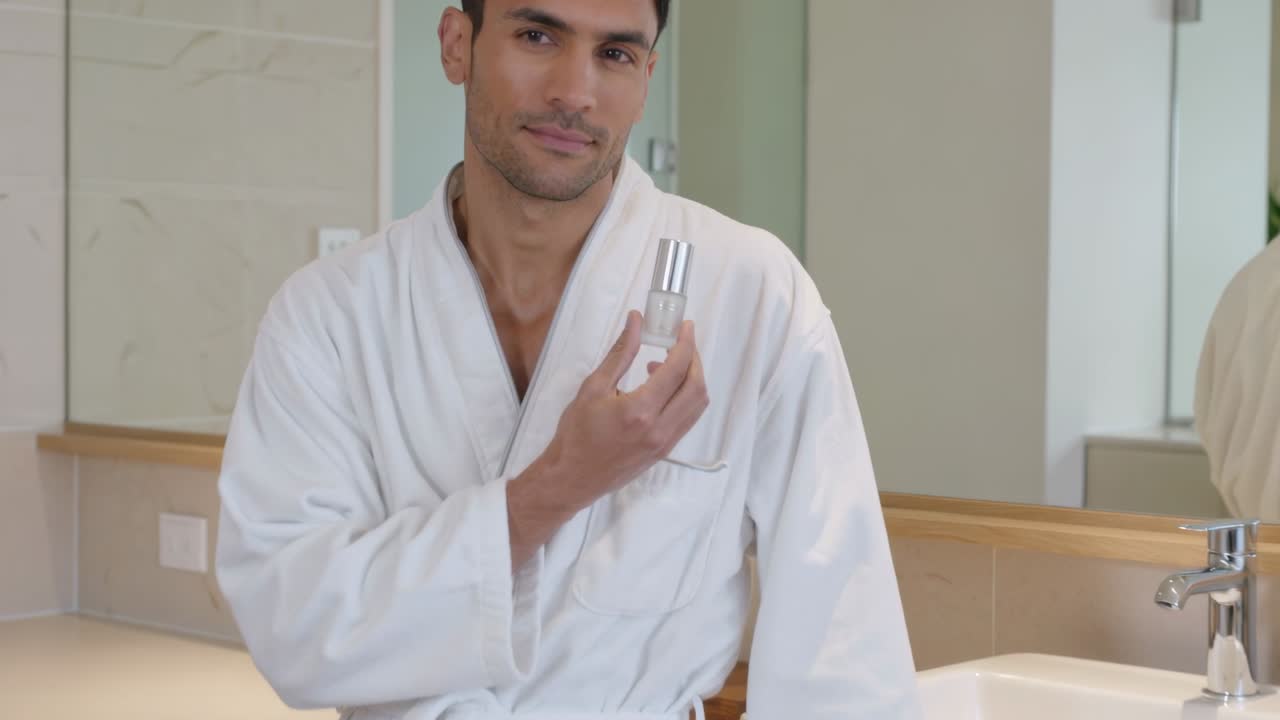 Showing man wearing white robe demonstrating serum to camera as camera tightening at vanity