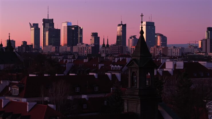 Drone establishing overview of Warsaw skyline at sunrise featuring Varso Tower, Q22 Building, and St Casimir Church