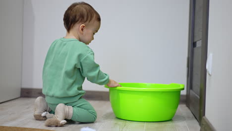 baby playing with a green plastic basin