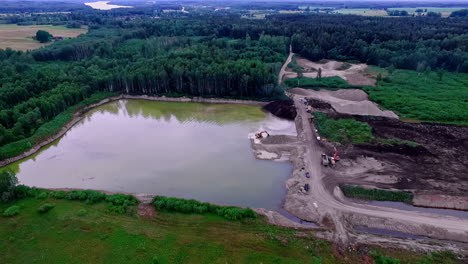 Hohe-Drohnenaufnahmen-Mit-Blick-Auf-Ein-Sand--Und-Kiesbergwerk-Neben-Einem-Großen-See-In-Lettland