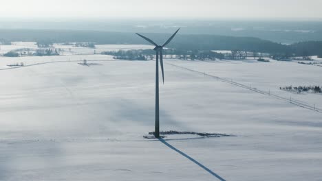 slow motion of a wind turbine rotating in a vast snowy landscape with distant trees and fields