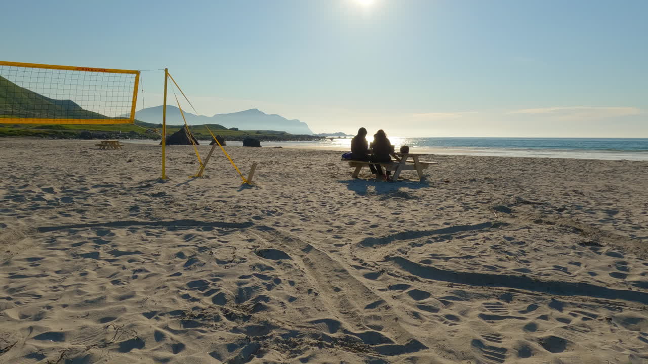 dos turistas disfrutando de la vista en la playa de flakstad, almorzando junto a la red de voleibol de playa