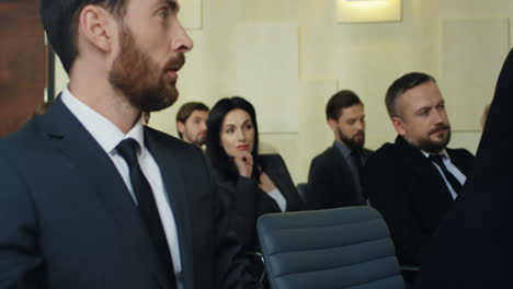 caucasian young businesswoman sitting on a empty chair among people in a conference room, next to her male colleague and showing him some documents which they discussing