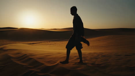 Silhouette of a person walking through desert dunes at sunset