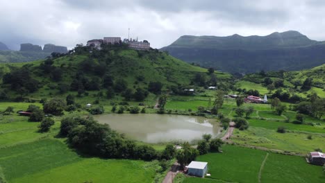 vista aérea del templo sagrado de nil parvat en los bordes de las colinas de brahmagiri con la vista de la ciudad de trimbakeshwar y las montañas sahyadri bajo un cielo nublado en el monzón, nashik, maharashtra, india