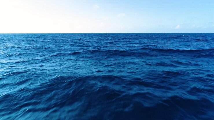 Avvicinamento aereo sopra un'onda oceanica rocciosa, texture dell'acqua blu profondo e orizzonte limpido