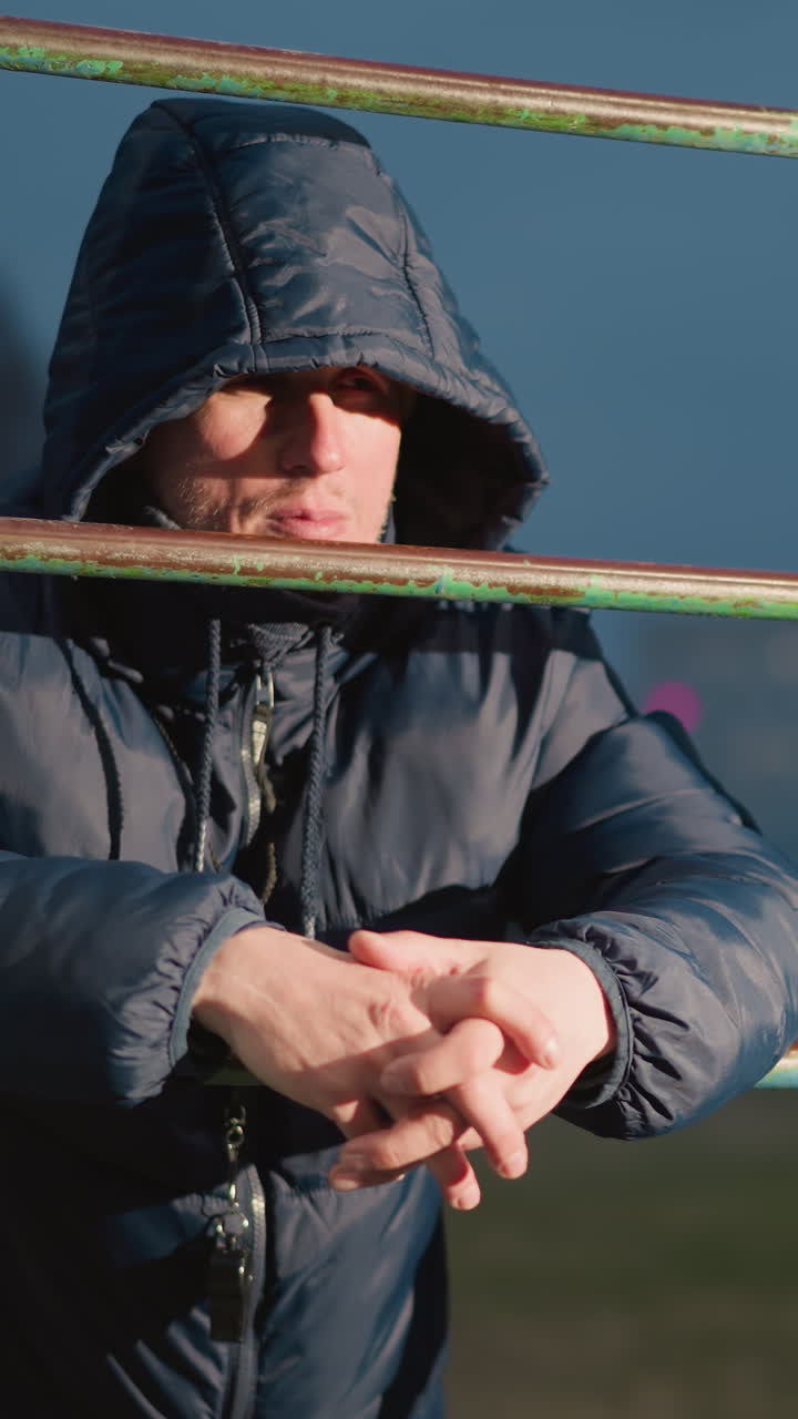 후드 재을 입은 사람이 철로 된 막대기에 손을 고, 배경에서 빛으로 조명되어 집중적으로 보이는 클로즈업