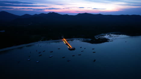 drone approaching illuminated loh jark pier, dusk in koh yao yai, thailand