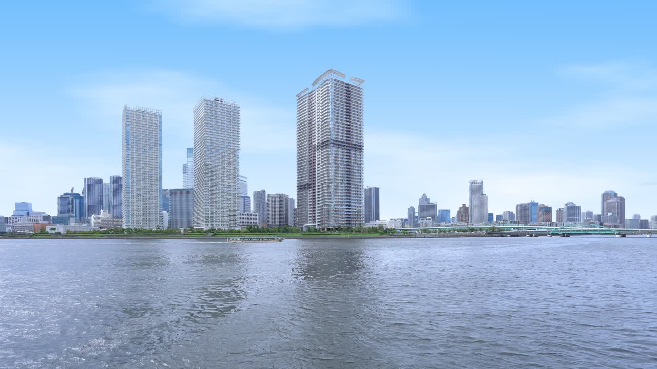A peaceful wide shot of the Tokyo skyline from the water, showing towering modern skyscrapers under a clear blue sky