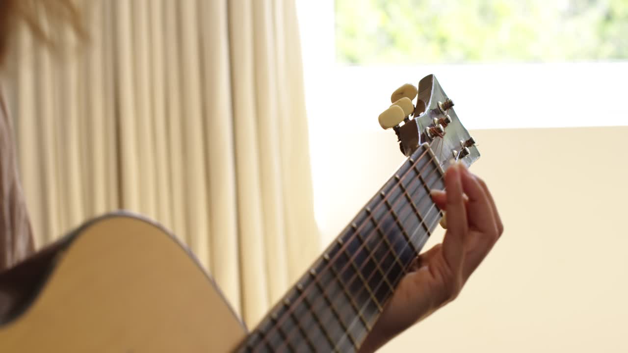 Donna afroamericana che pratica la chitarra acustica, muovendo la mano sinistra lungo la tastiera per imparare una canzone