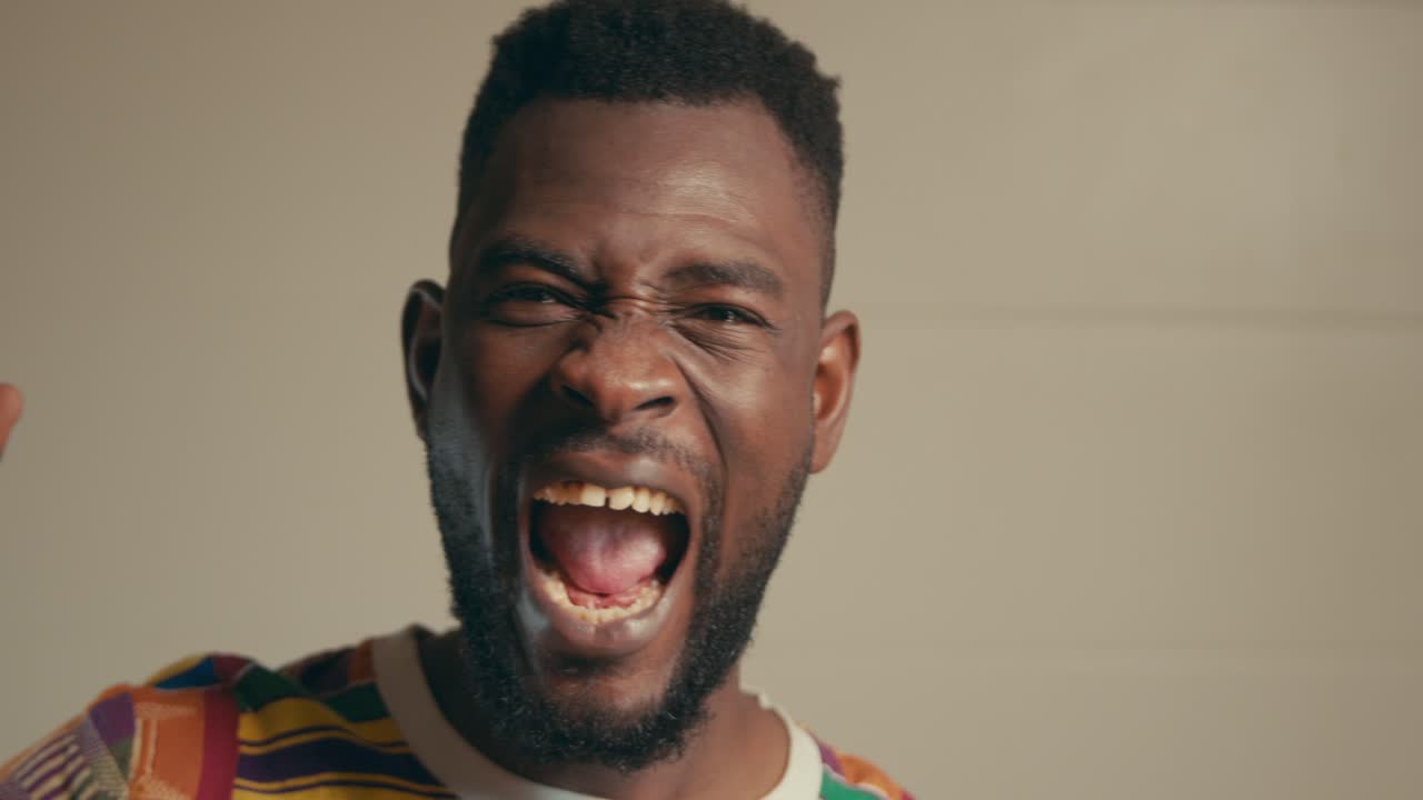 Portræt af afroamerikansk mand iført Kente-stofskjorte, der fejrer begejstret i slowmotion.