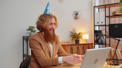 Happy-business-office-man-wears-festive-birthday-hat-hold-cupcake-makes-wish-blowing-burning-candle