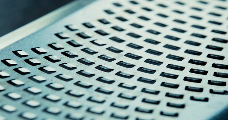 A macro shot of a metal cheese grater showing sharp blades and texture. Useful for cooking tutorials, food industry backgrounds, and kitchenware product videos.