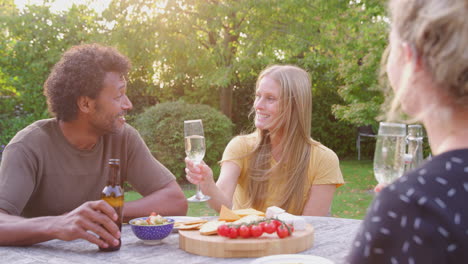 group of friends celebrating with beer and champagne as they sit at table in garden with snacks