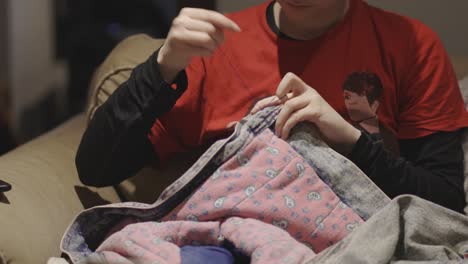 a person wearing red shirt stitching a button on the gray and pink colored clothing