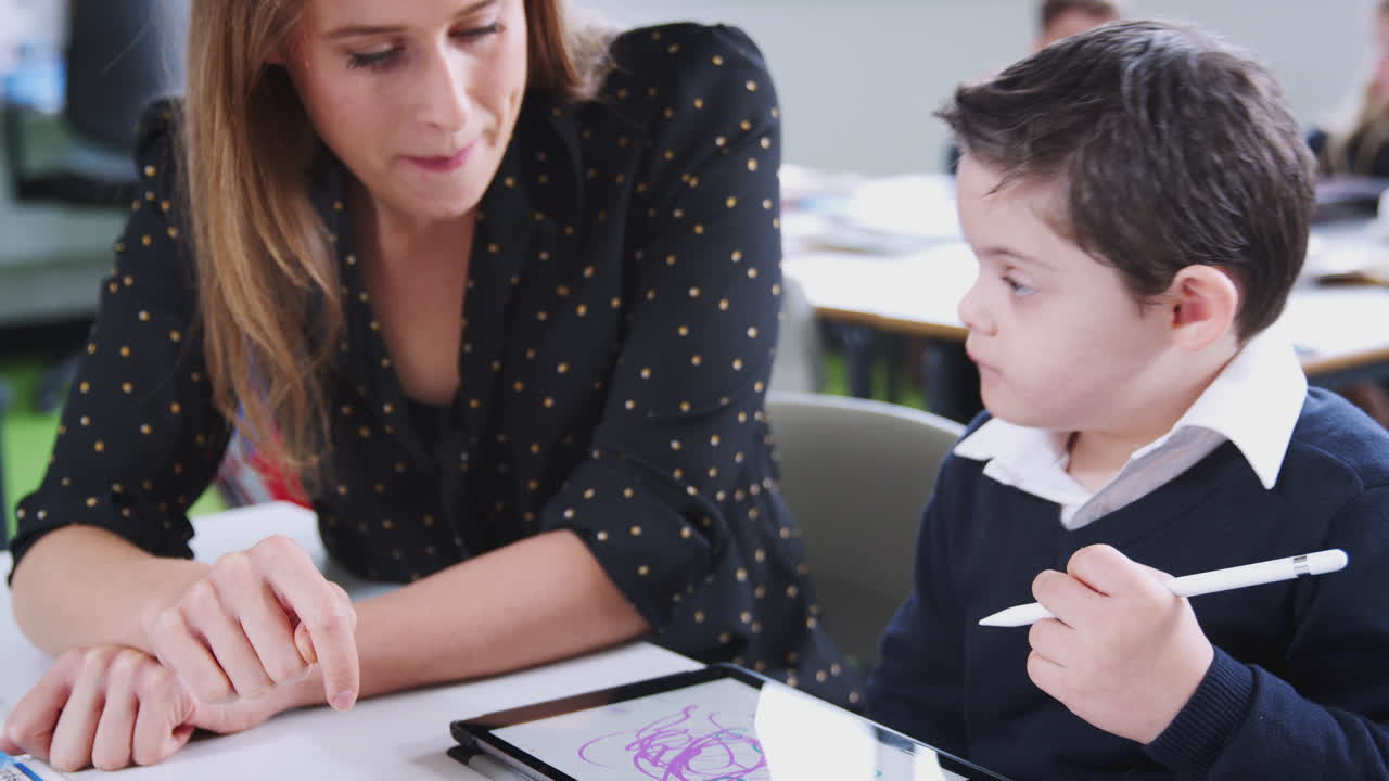 maestra trabajando con un niño con síndrome de down usando una tableta en una clase de escuela primaria, de cerca