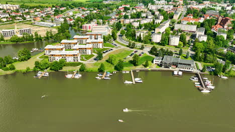 Aerial-view-of-Iława,-featuring-modern-residential-buildings-along-the-lake,-a-marina-with-boats,-and-the-surrounding-lush-green-landscape,-capturing-a-serene-town-vibe