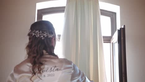 bride in gown admiring her wedding dress hanging from ceiling beam