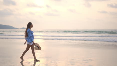 young asian woman walks on seashore at sunset