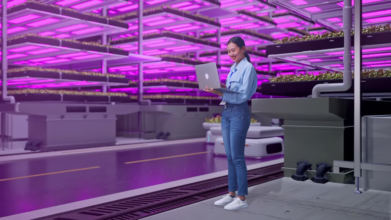 Full Body Side View Of An Asian Female Professional Worker Standing With Her Laptop In Vertical Farm, High-tech Industrial Facility, Typing On Her Laptop'S Keybaord With Meditation