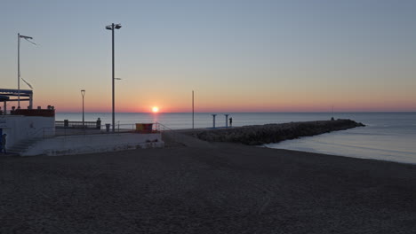 time-lapse captures majesty of sunrise as it illuminates pier stretching out into sea, with sun rising from a white building in harbour.