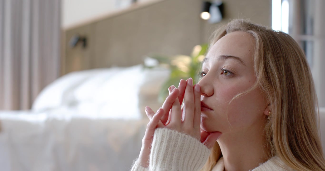Adult female at home wearing chunky knit, hands clasped, opening eyes to light, focusing