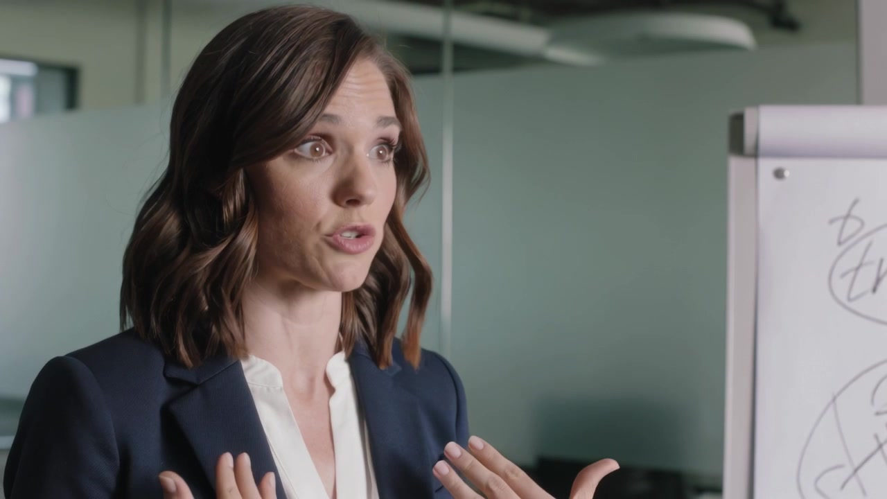 Starting woman in navy blazer and white blouse presenting plan in office, referencing flipchart