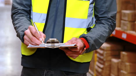 Mid-section-of-warehouse-worker-writing-on-clipboard