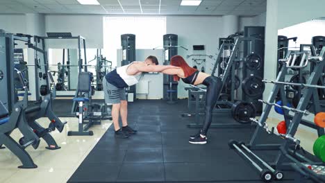 young couple is doing exercise together in a sport center. sportive girl and strong man are holding their hands on friend's shoulders keeping balance while exercising in health club.