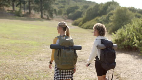 two women with backpacks hike in a grassy outdoor setting