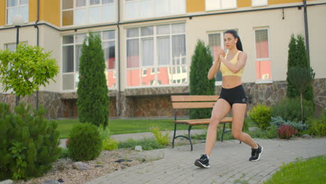 a woman makes lunges on a sidewalk path in a park in an urban environment. slow-motion shooting of a woman in sportswear steps with a lunge