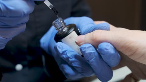 Woman-having-a-nail-manicure-in-a-beauty-salon-with-a-closeup-view-of-a-beautician-applying-varnish-with-an-applicator