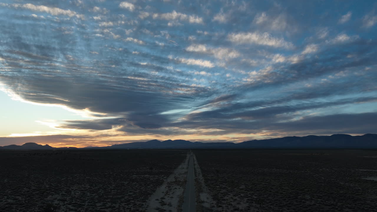 camino del desierto que se extiende hacia el horizonte bajo un vasto cielo con nubes dramáticas al anochecer, desierto de mojave, time-lapse