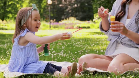 Madre-Con-Hija-Soplando-Pompas-De-Jabón-En-El-Parque.concepto-De-Familia,-Maternidad-Y-Personas-Madre-Feliz-Con-Hija-Pequeña-Soplando-Pompas-De-Jabón-En-El-Parque-O-Jardín-De-Verano