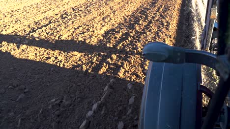 tractor driving on the side of plowed field, view from cabin on front wheel
