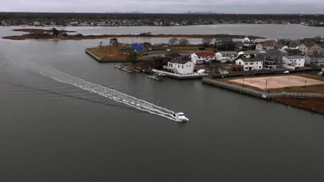 Una-Vista-Aérea-De-Un-Pequeño-Barco-Blanco-En-La-Bahía-Frente-A-La-Costa-Sur-De-Freeport,-Nueva-York-En-Un-Día-Nublado