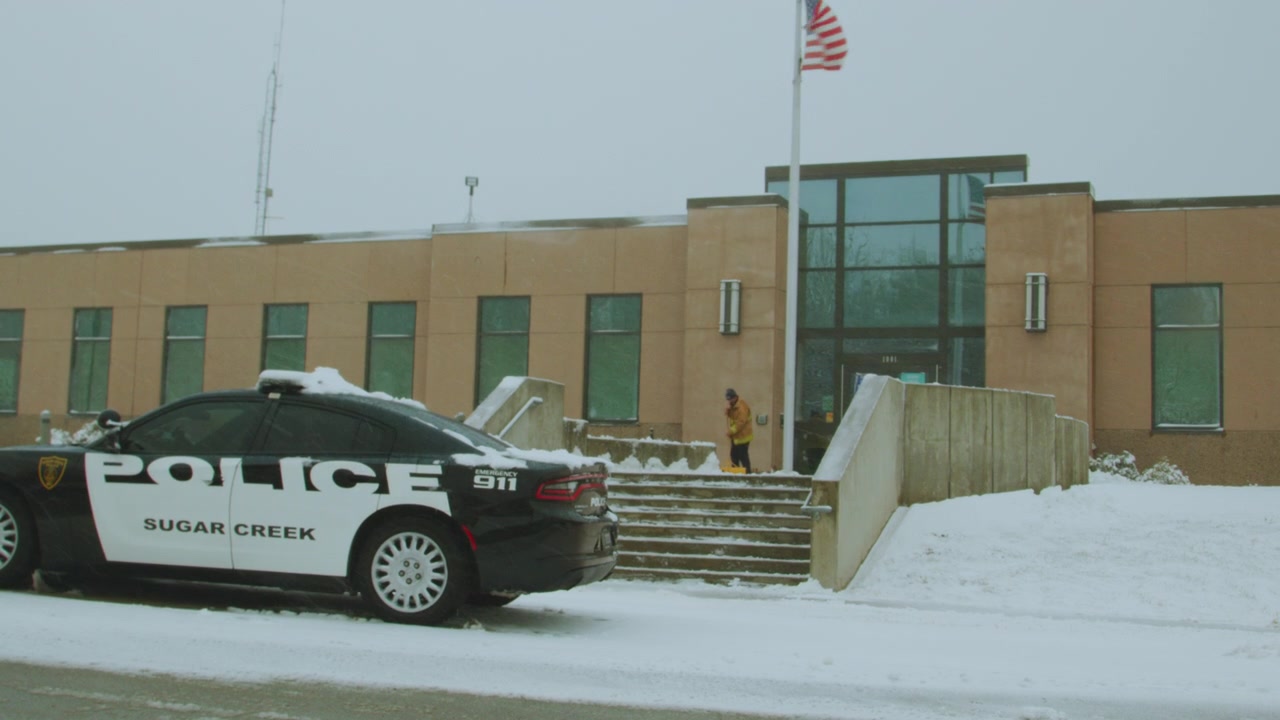 Utsikt over en politistasjon i Colorado, USA med en politibil parkert foran bygningen. USAs flagg vaier på en kald vintermorgen